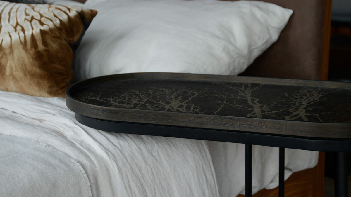 Ethnicraft lozenge shape side table shown over a bed and with removable tray