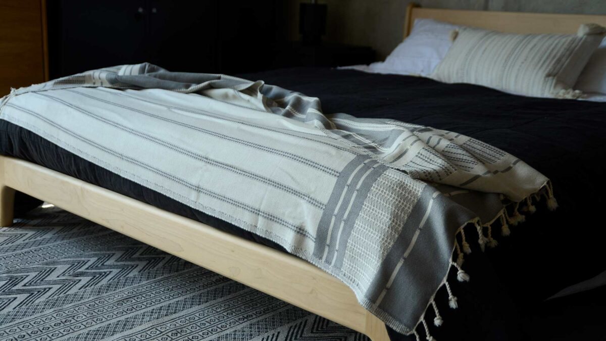 reversible woven cotton Turkish throw in ivory and grey shown on a low oak bed