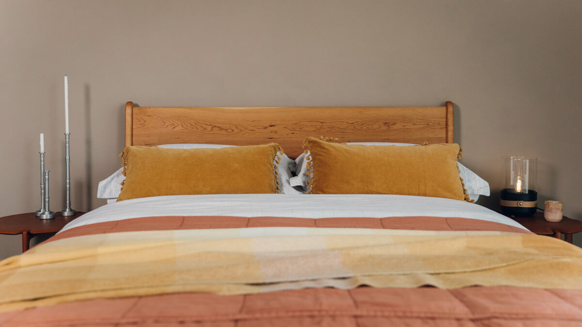 rectangular ochre coloured velvet cushions with tasselled edges shown on a bed