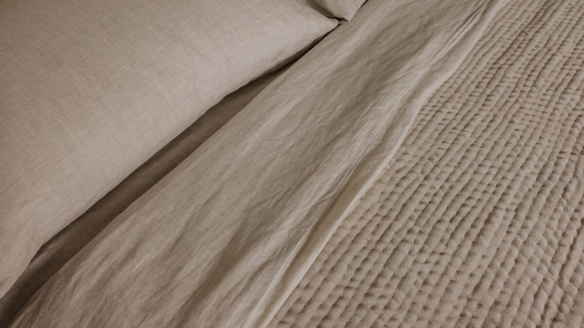 Close up view of the stitched velvet bedspread in soft beige on top of the organic ecru linen bedding.