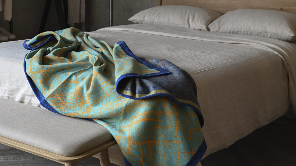 Vibrant green and blue throw with mustard slash pattern, messily spread on stone bedding.