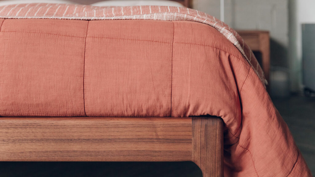 quilted cotton bedspread in terracotta on a walnut Camden bed shown in close up