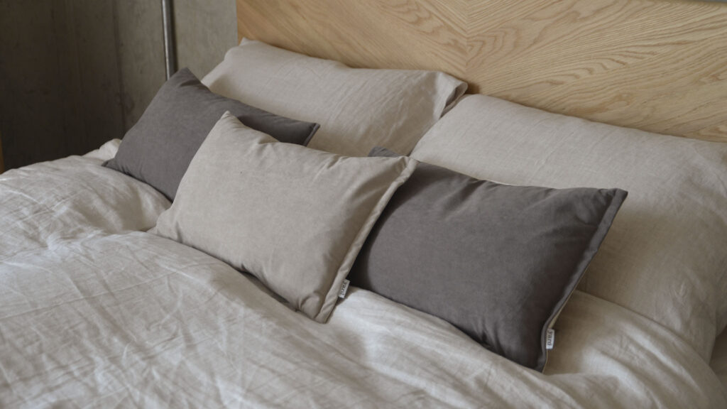 beige linen bedding with grey and beige velvet cushions.