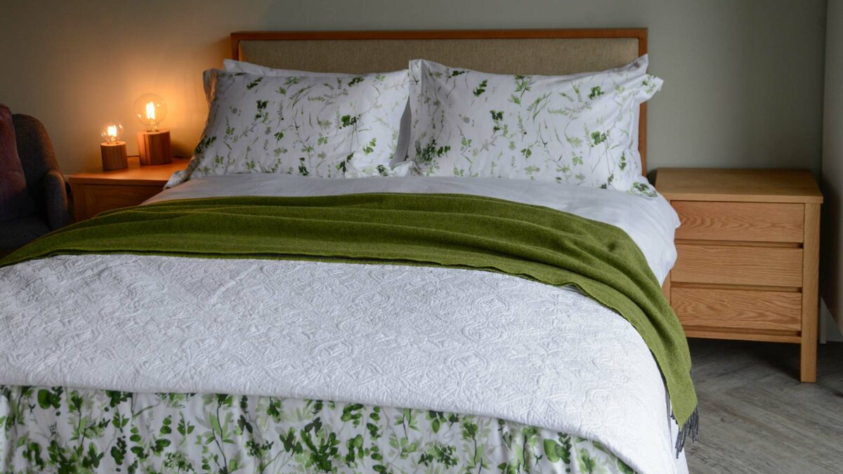 embroidered white quilted bedspread shown with bedding accents of green