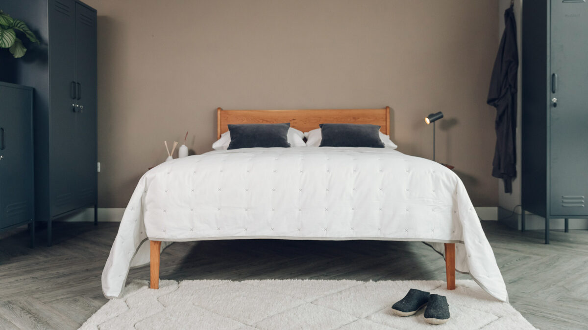 white cotton quilted bedspread with grey cross stitch details shown on a kingsize cherry wood bed