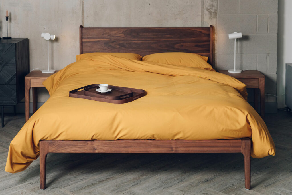 deep walnut wood hand crafted Camden bed with an oiled finish shown with yellow ochre bedding