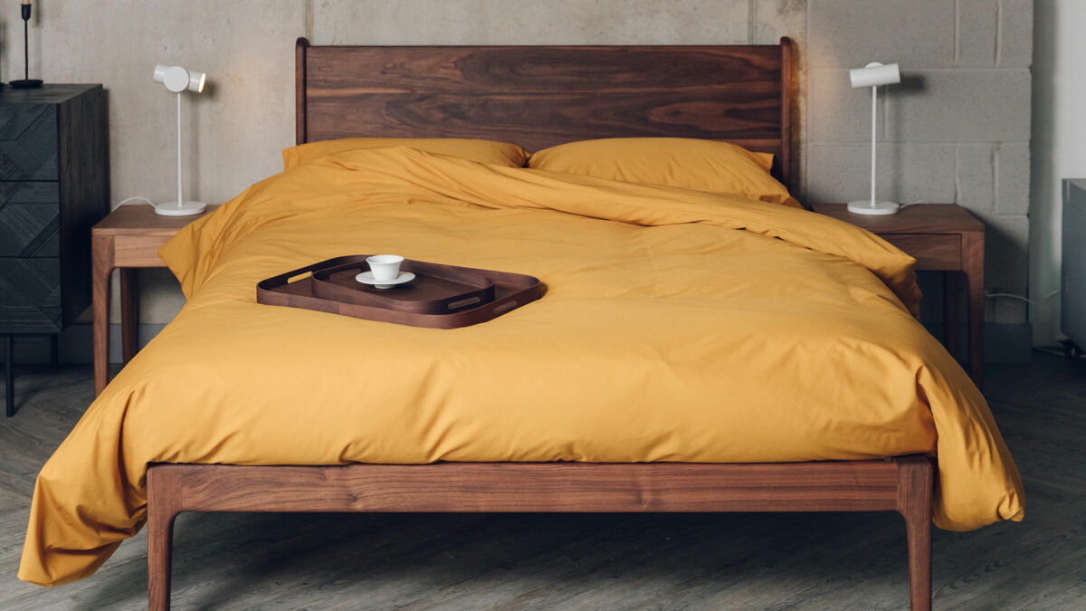 deep walnut wood hand crafted Camden bed with an oiled finish shown with yellow ochre bedding